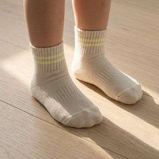 A toddler's feet in undyed STROMA socks in a sunbeam on a wooden floor