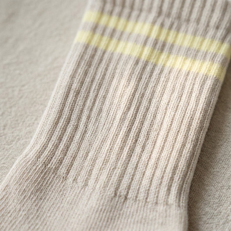 Macro detail of the STROMA sock cuff — undyed greige rib knit with two pale yellow stripes