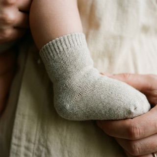 A parent's hand holding a toddler's foot in a Unit 02 sock
